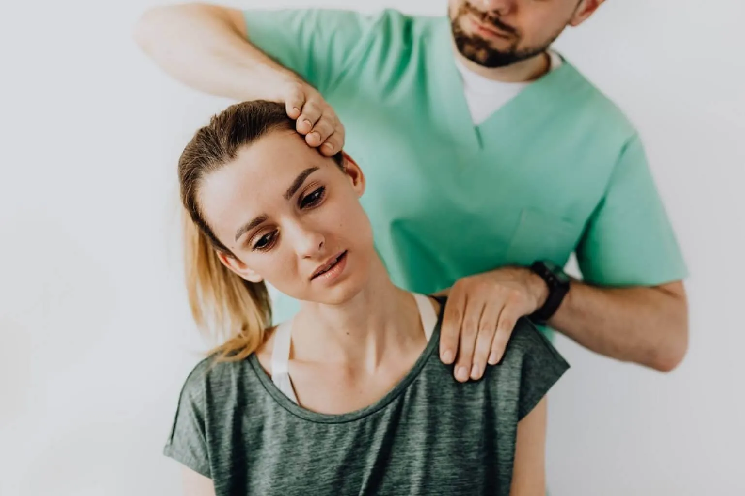 穿綠色刷手服的治療師站在後方,一手扶住女性頭部側邊、一手壓住肩膀,帶她把頸部往側邊傾斜